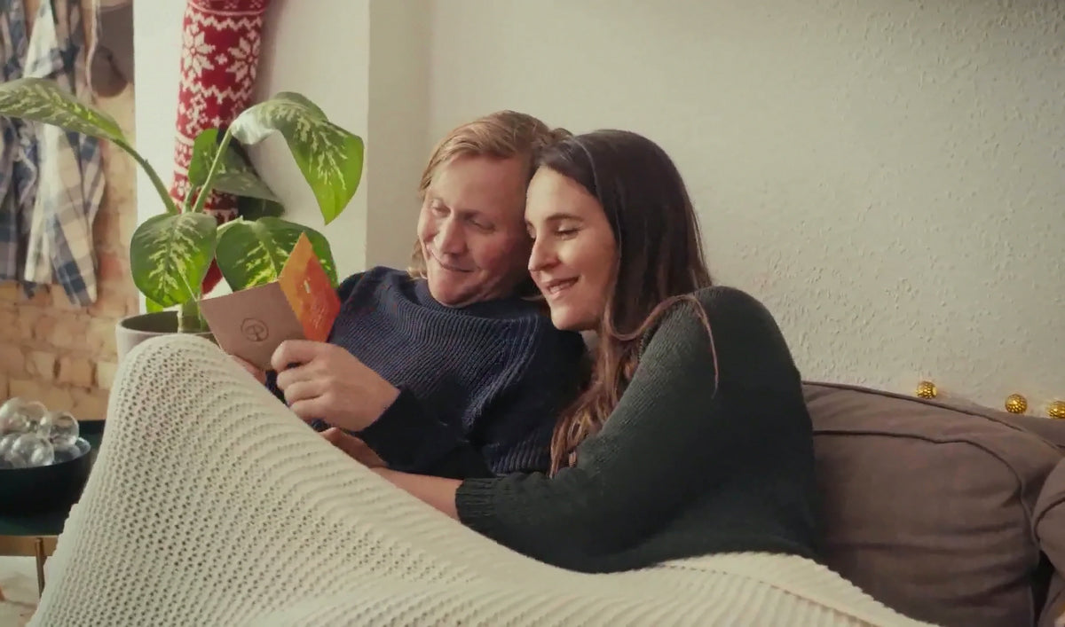 Un couple lit ensemble une carte du calendrier de l'Avent COUPle DE CŒUR, blottis sous un plaid